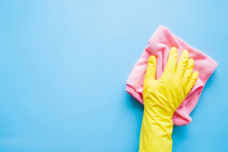 Does an AC Kill Mold? Hand in a yellow rubber glove wiping a blue wall or table with a pink cloth.